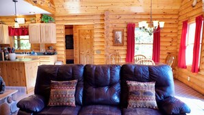 A log cabin interior with a leather sofa, wooden walls, a kitchen area, and a dining table.
