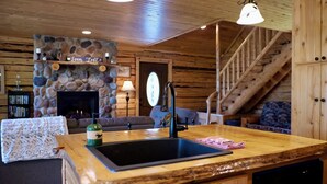 Ein gemütliches Blockhaus-Interieur mit Kamin aus Stein, Holzbalkendecke und einem Essbereich mit Spüle und Bar.