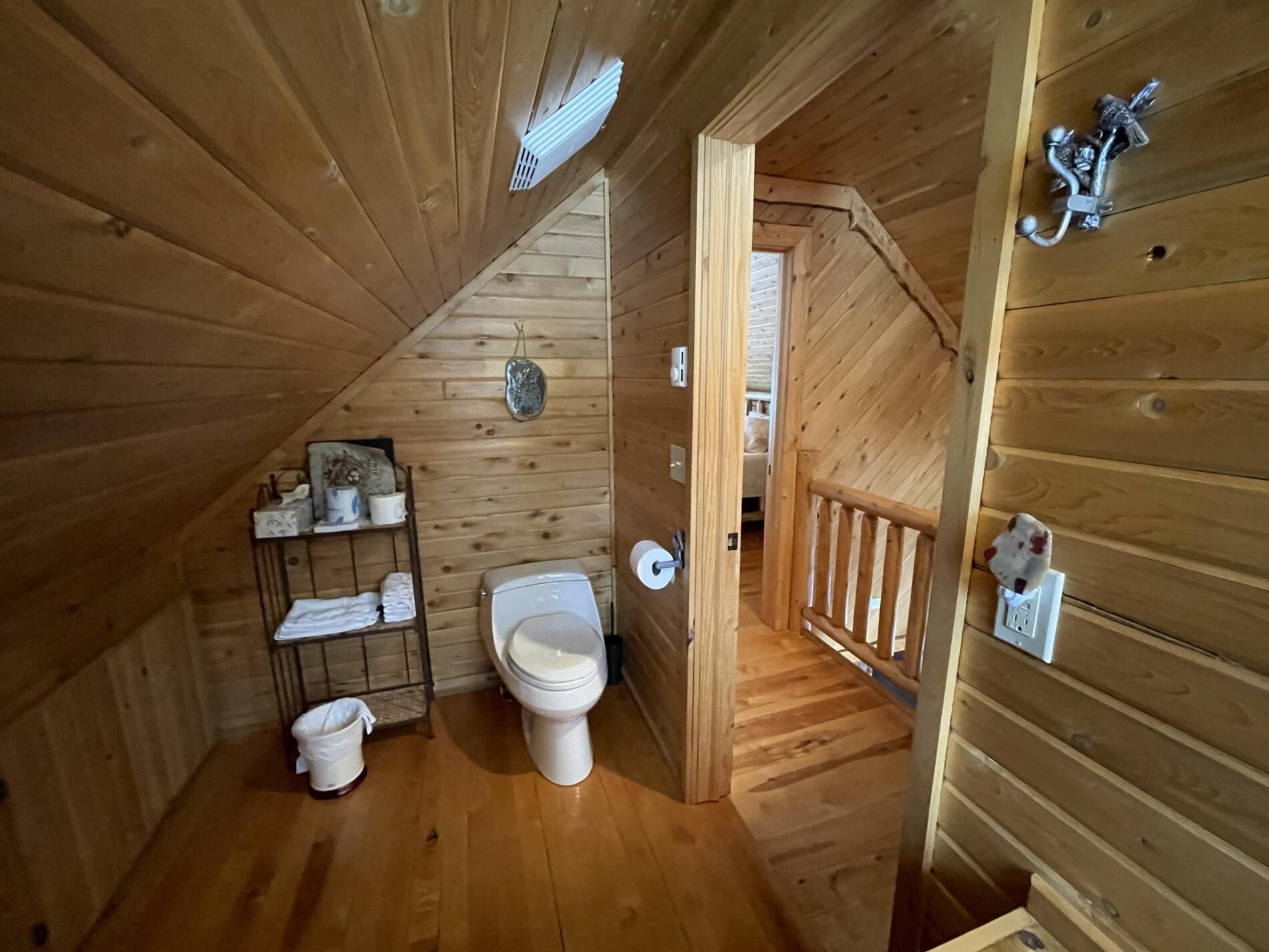 Baño de una cabaña de madera pequeña con inodoro, lavamanos y un estante con artículos de tocador.