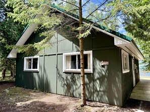 Un petit bâtiment d’un seul étage, à l’extérieur vert et aux bordures blanches, entouré d’arbres.