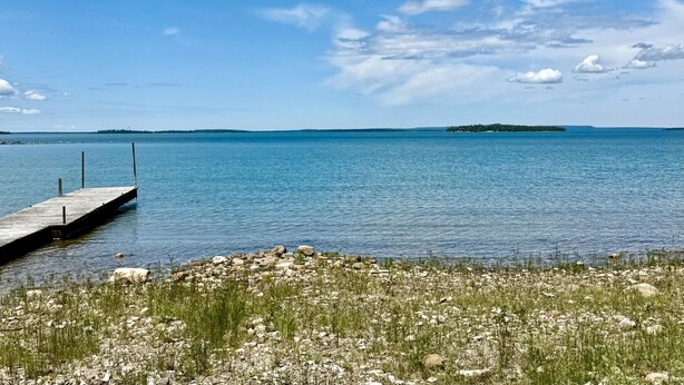 Un lago tranquilo con un muelle que se adentra en el agua, rodeado por una orilla rocosa con vegetación escasa.