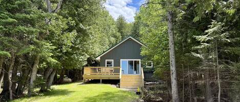 A cabin with a deck, surrounded by dense forest.
