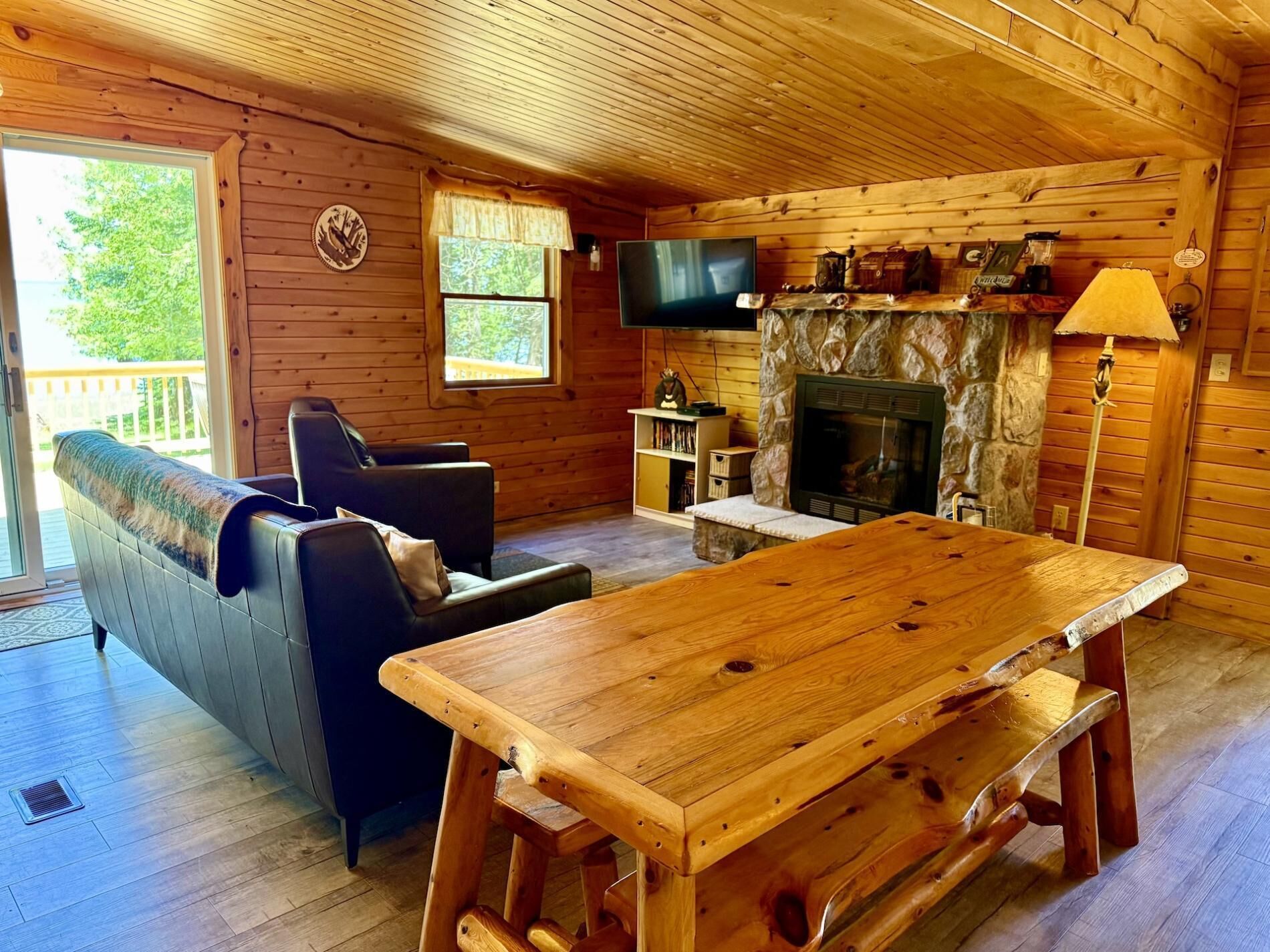 A wooden cabin interior with a sofa, a wooden table, a fireplace, and a television.