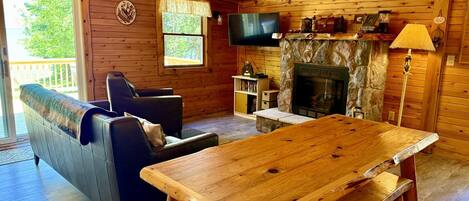 A wooden cabin interior with a sofa, a wooden table, a fireplace, and a television.
