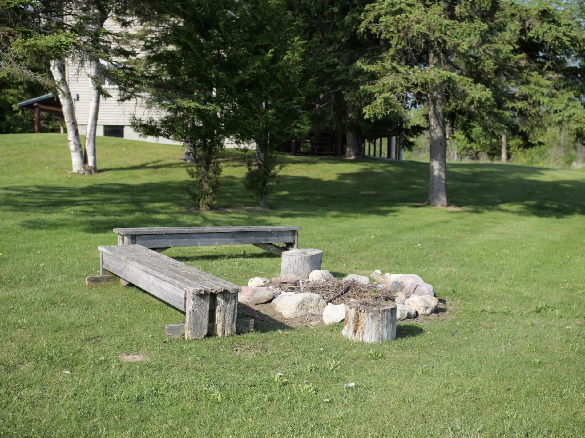 A wooden bench in a grassy area with trees and a building in the background.