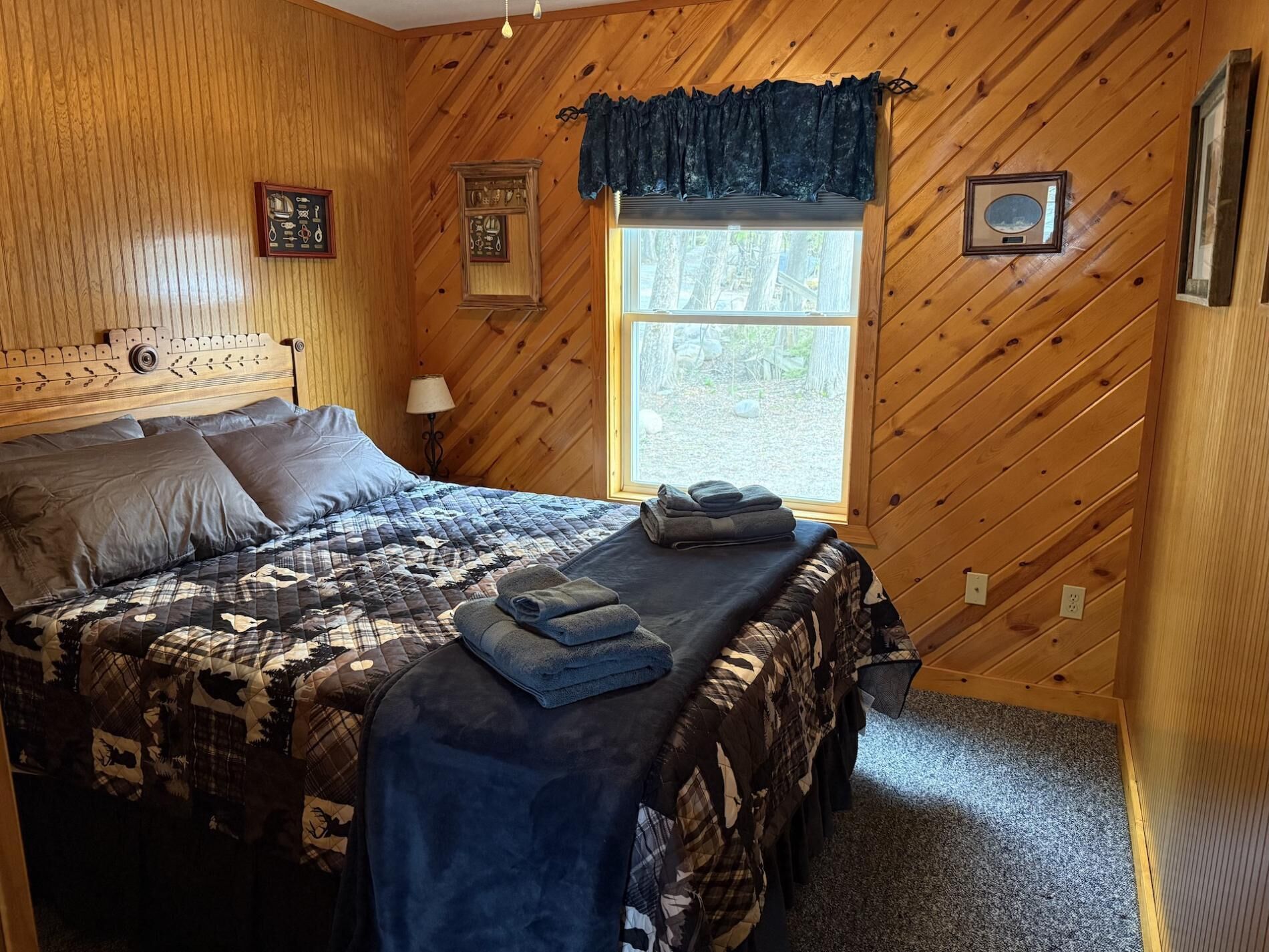 A wooden paneled room with a bed, a window, and a nightstand.