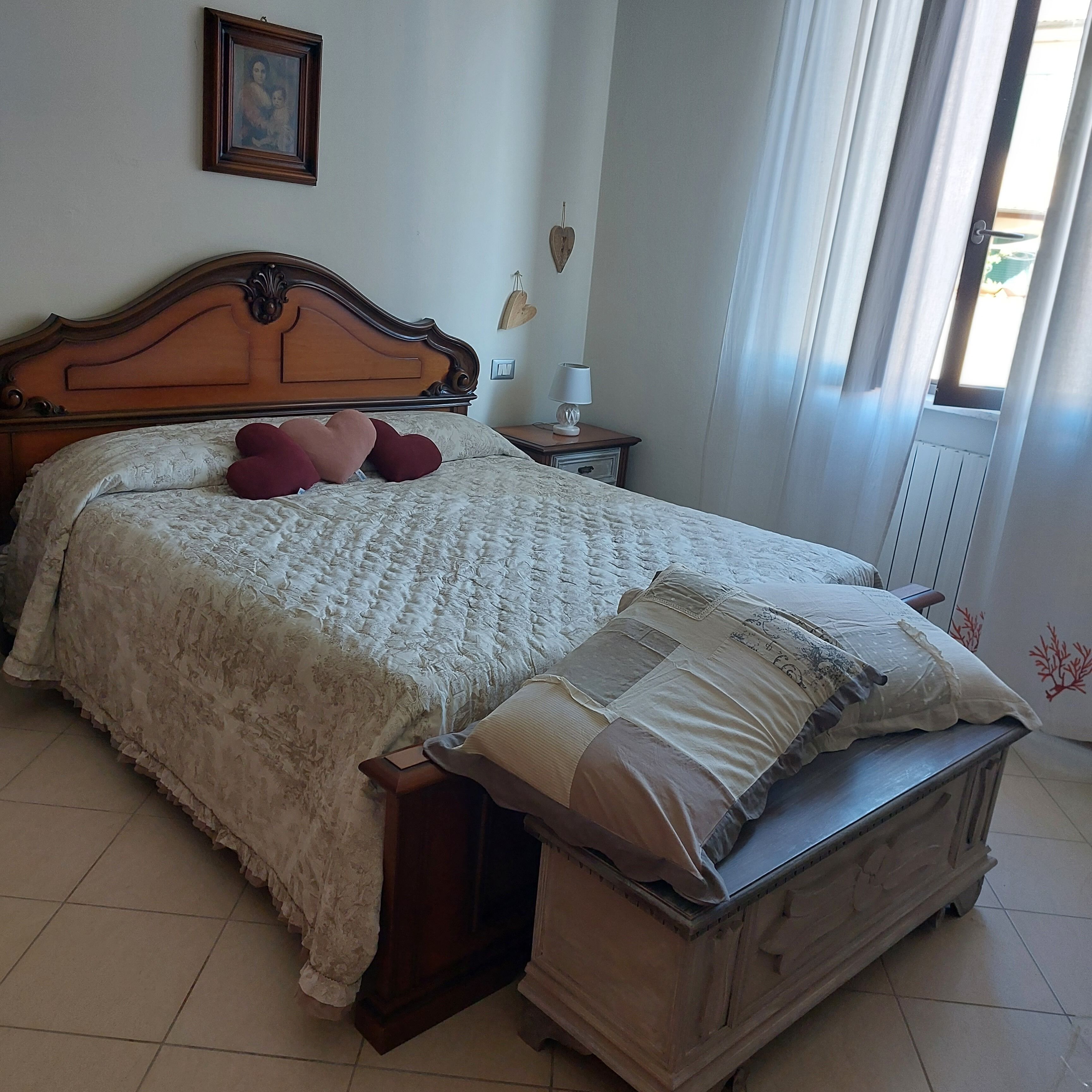 Una camera da letto con un letto di legno, un comodino, una lampada e una finestra con tende.