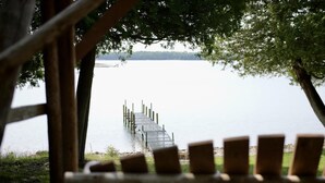 A wooden pier extending into a calm lake, viewed through a wooden structure with a bench in the foreground.