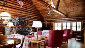 A cozy cabin interior with a stone fireplace, plaid furniture, and wooden beams.