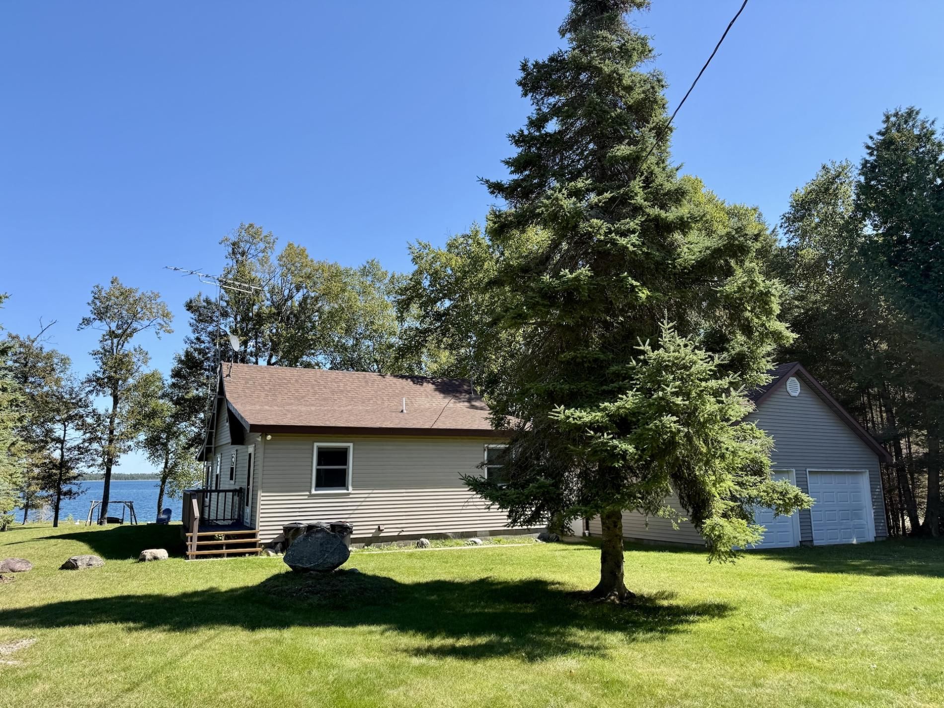 A house with a front porch, a garage, and a large tree in the yard.