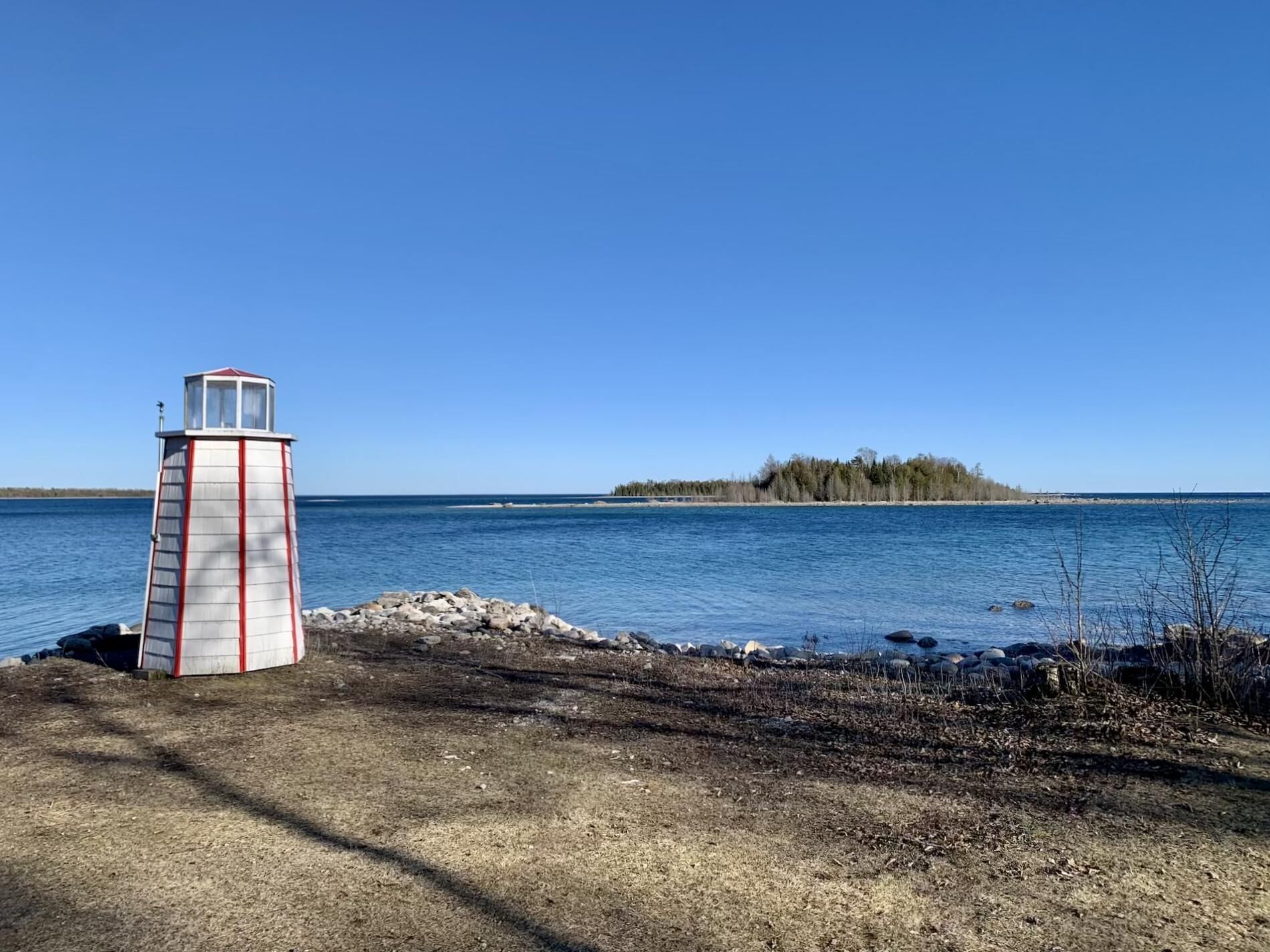 Un phare se dresse sur une côte rocheuse, offrant une vue dégagée sur une île lointaine.
