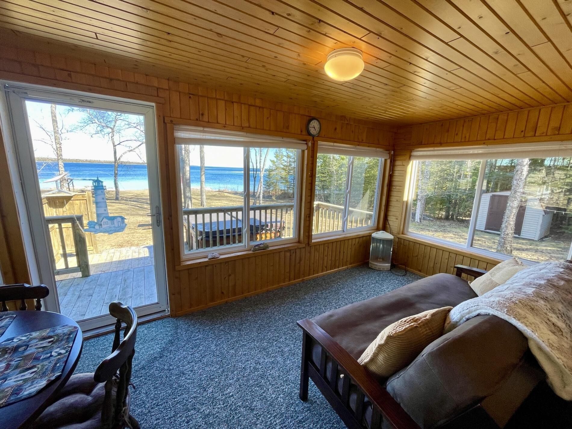 A cozy cabin with a wooden interior, large windows offering a view of the beach and ocean, a comfortable seating area with a sofa and a table.
