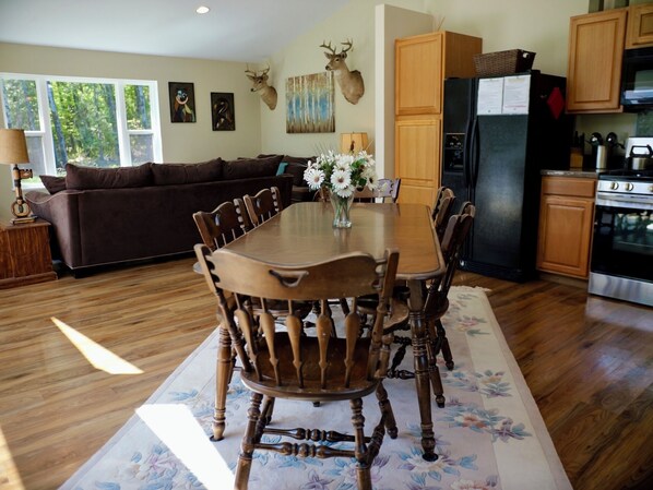 Un comedor con una mesa y sillas de madera, un tapete floral, un sofá y una cocina con armarios y electrodomésticos de madera.
