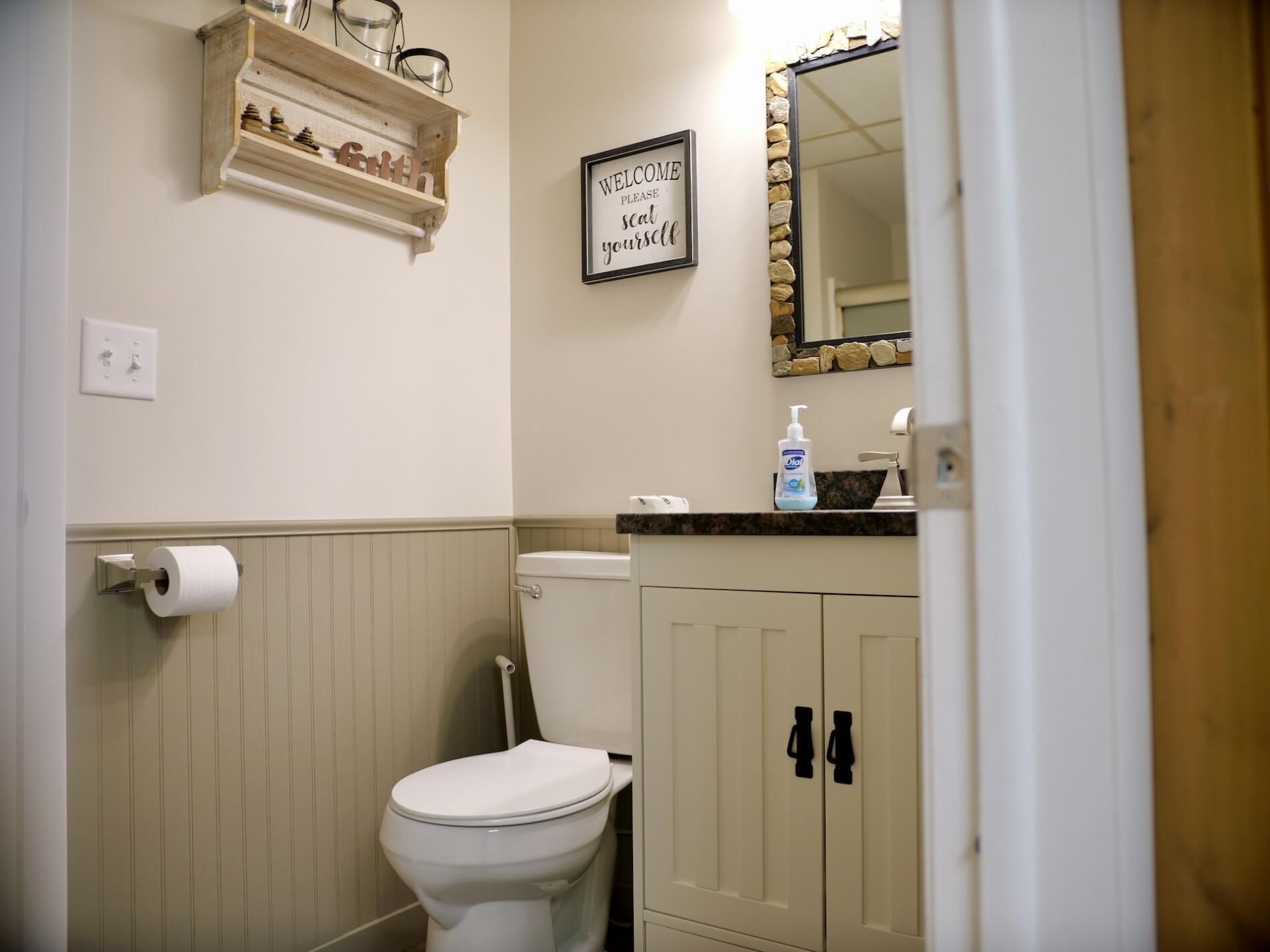 Un baño con inodoro, dispensador de jabón, espejo con marco de piedra y porta rollos.