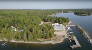 An aerial view of a lakeside property with a dock, a small building, and a boat storage area.