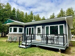 A single-story house with a covered porch, a small deck, and a stone foundation. - Dockside on Drummond Island (Drummond Island)