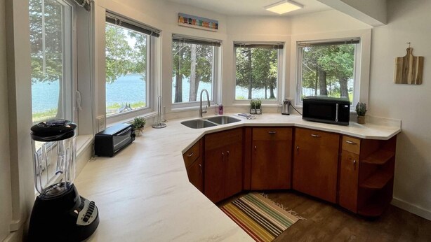 Une cuisine moderne dotée d’un îlot central aux lignes courbes, de grandes fenêtres et d’une vue sur un lac.