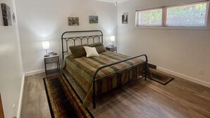 Une chambre à coucher comprenant un lit, un ventilateur de plafond, une fenêtre avec des stores et une table de chevet avec une lampe.