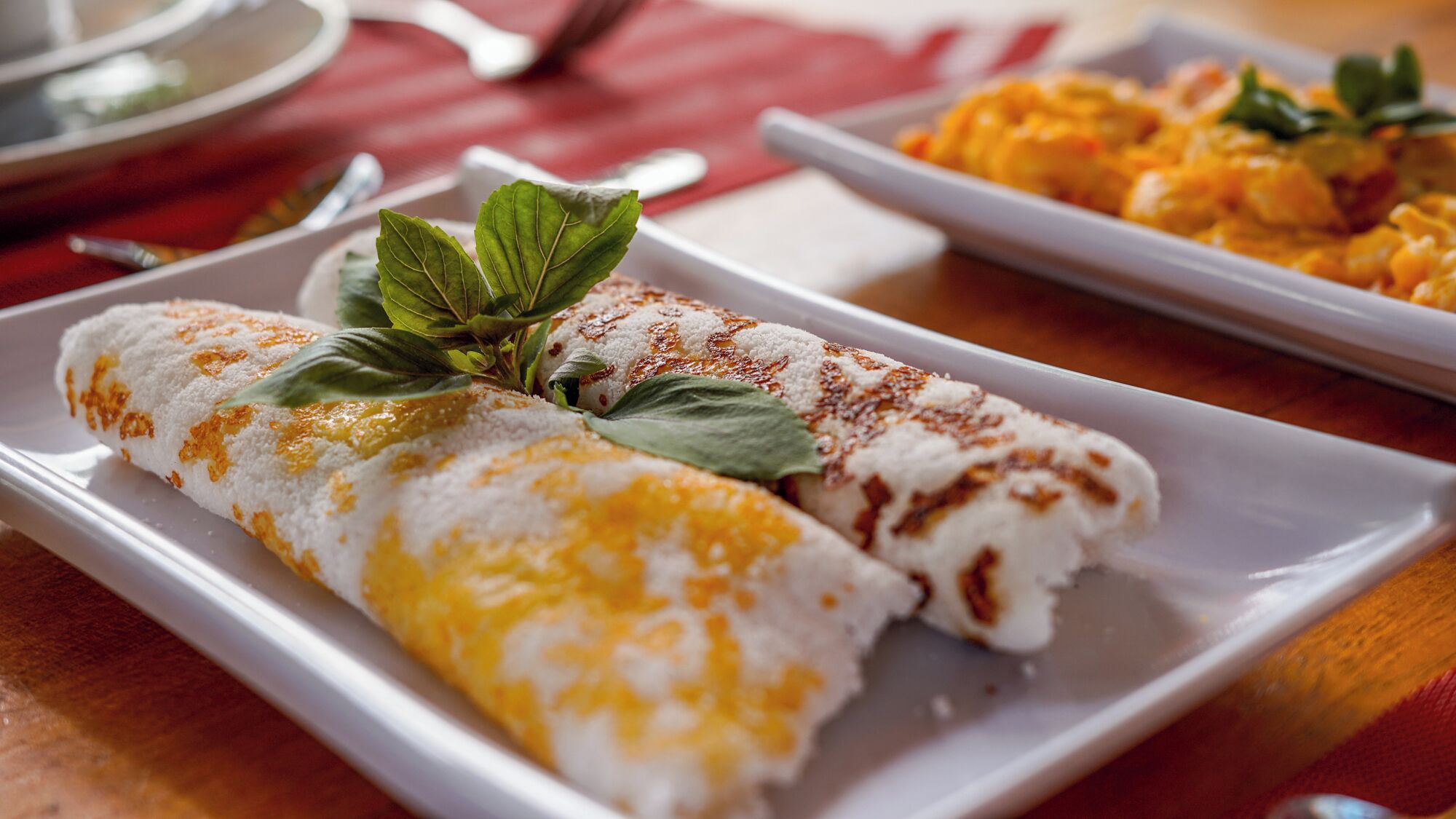 Un plato con dos bollos enrollados decorados con una hoja, y otro plato con un plato diferente al fondo.