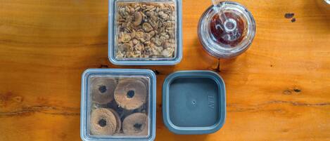 Three clear plastic containers with food items, a glass jar with a dark liquid, and a gray lid on a wooden surface.
