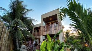 A two-story building with a balcony, surrounded by tropical plants and a brick pathway. - Pousada Brisas de Sagi (Baia Formosa)