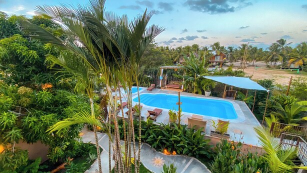 A swimming pool surrounded by lush greenery, with a covered seating area and a view of the beach. - Pousada Brisas de Sagi (Baia Formosa)