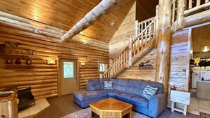A log cabin interior with a wooden staircase, a blue sectional sofa, and a small wooden table. - Paw Point Lodge on Drummond Island (Drummond Island)