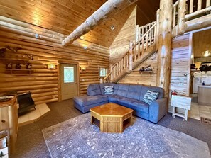 L’intérieur d’une cabane en rondins, avec un escalier en bois, un canapé d’angle bleu et une petite table en bois.