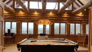 A pool table in a room with wooden beams and large windows. - Paw Point Lodge on Drummond Island (Drummond Island)