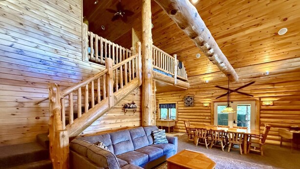 A log cabin interior with a wooden staircase, a sofa, a dining table with chairs, and a ceiling fan. - Paw Point Lodge on Drummond Island (Drummond Island)