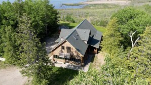 A wooden cabin with a sloped roof, surrounded by dense trees and a lake in the background. - Paw Point Lodge on Drummond Island (Drummond Island)