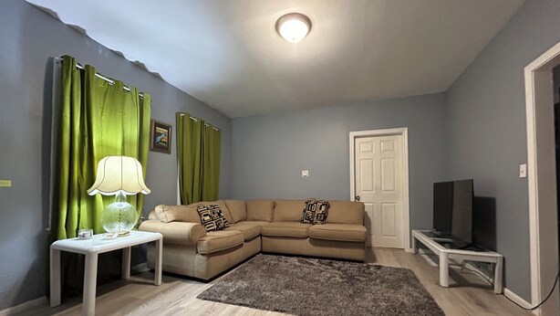 Un salon avec un canapé, une petite table sur laquelle se trouve une lampe, un téléviseur et une porte.