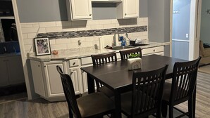 Une cuisine de taille réduite avec des meubles blancs, une table à manger en bois foncé et un revêtement mural en carreaux.