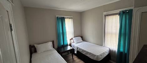 Una habitación pequeña y limpia con dos camas individuales, un escritorio y una silla.