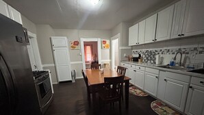 Une cuisine avec des meubles blancs, une table à manger en bois et un réfrigérateur.