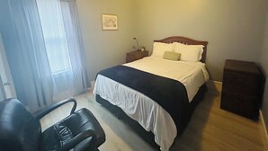 Une chambre d’hôtel avec un lit, un bureau, une chaise, une table de chevet et une fenêtre avec des rideaux.