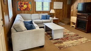A cozy living room with a sectional sofa, a coffee table, a fireplace, and a television.