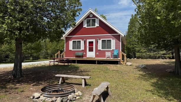 A red cabin with a porch, a fire pit, and a bench.