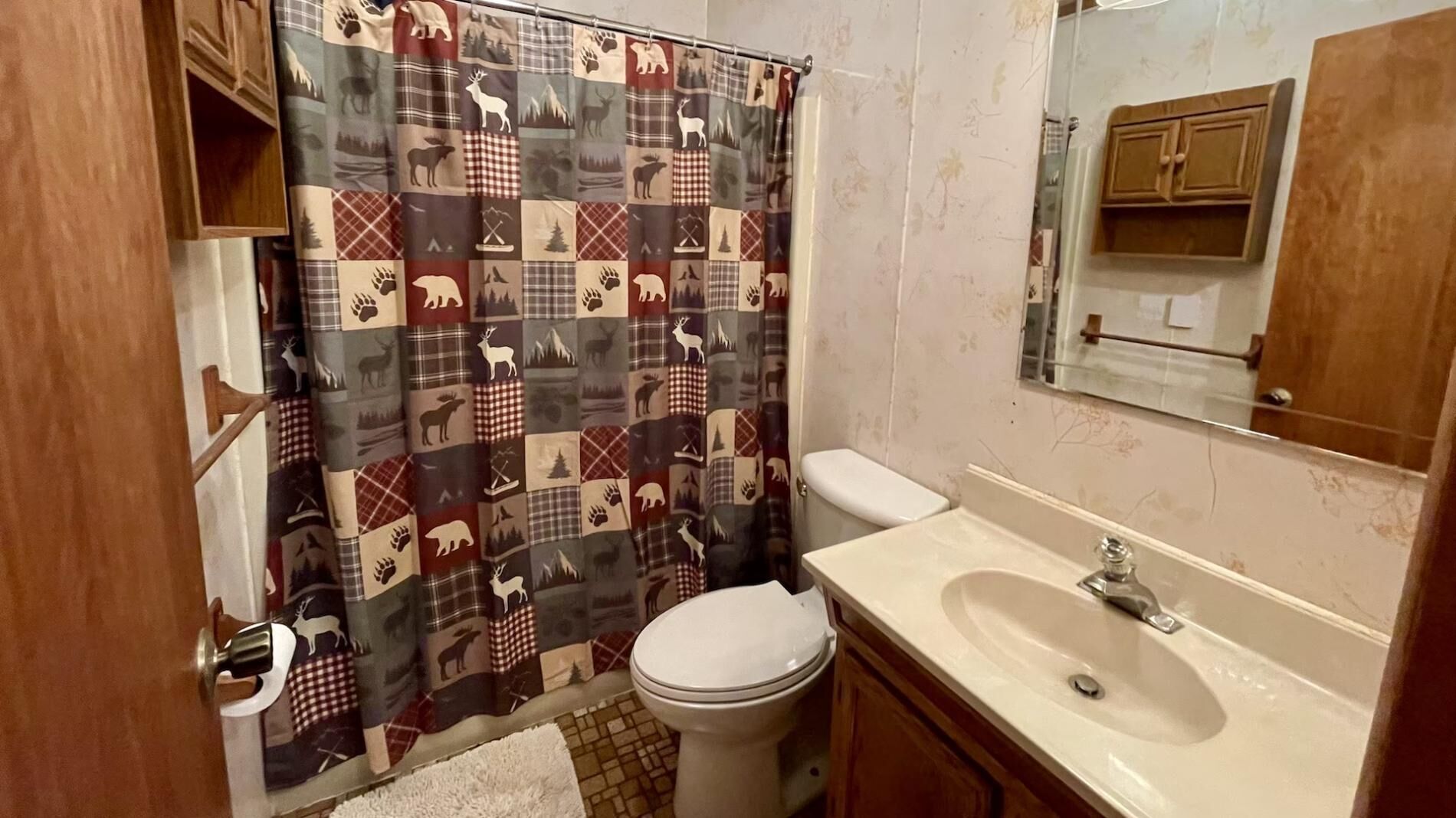 A bathroom with a plaid shower curtain, a toilet, a sink, and a mirror.