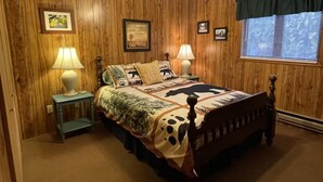 A wooden-paneled bedroom with a bed featuring a dog-themed bedspread, two bedside lamps, and framed pictures on the walls.