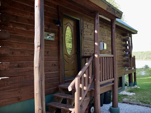 A wooden cabin with a porch, a welcome sign, and a view of a lake.