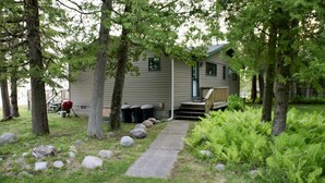 A cabin with a porch, surrounded by trees and a grassy area with rocks.