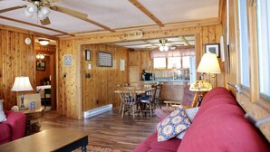A cozy cabin interior with a dining area, kitchen, and a living room with a red sofa and a table.