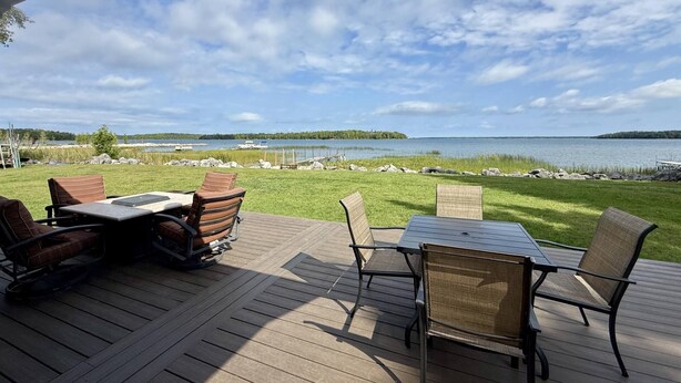 Una terraza al aire libre con una mesa y sillas, con vistas a un lago con barcos y una isla distante.