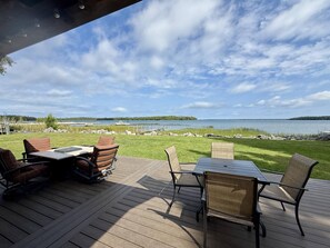 An outdoor deck with a table and chairs, overlooking a lake with boats and a distant island. - Lakeside Ranch on Drummond Island (Drummond Island)