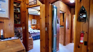 Un interior de madera con un escritorio, estanterías, una cama y un extintor.