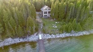 Eine Luftaufnahme einer Hütte, umgeben von dichtem Wald, mit einem Steg, der in einen stillen See führt.