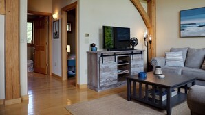 Ein gemütliches Wohnzimmer mit Holzboden, einem Fernseher auf einer Holzkommode, einem grauen Sofa und einem Couchtisch.
