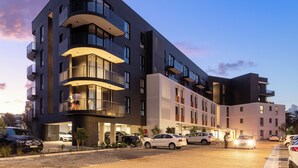 A multi-story hotel with a modern design, featuring balconies, a parking area, and a well-lit entrance.