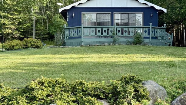 Une maison de plain-pied à l’extérieur bleu et au toit blanc, entourée d’une pelouse bien entretenue et d’arbres.